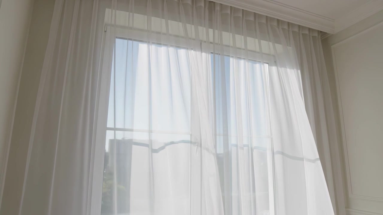Brisa levantando cortinas transparentes, movendo-se pela janela de vidro na sala de estar, revelando o corrimão.