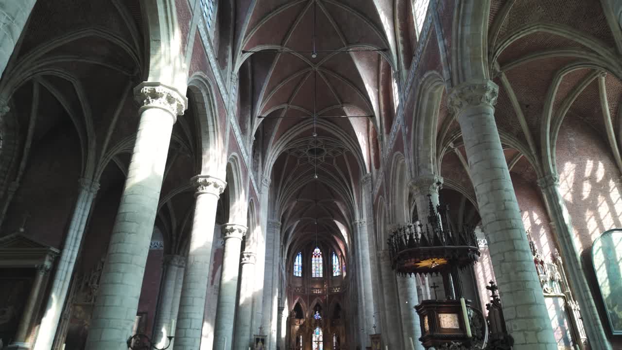 Sunlight illuminates the tall columns and pulpit inside the gothic saint michael's church in ghent, belgium, creating a serene atmosphere