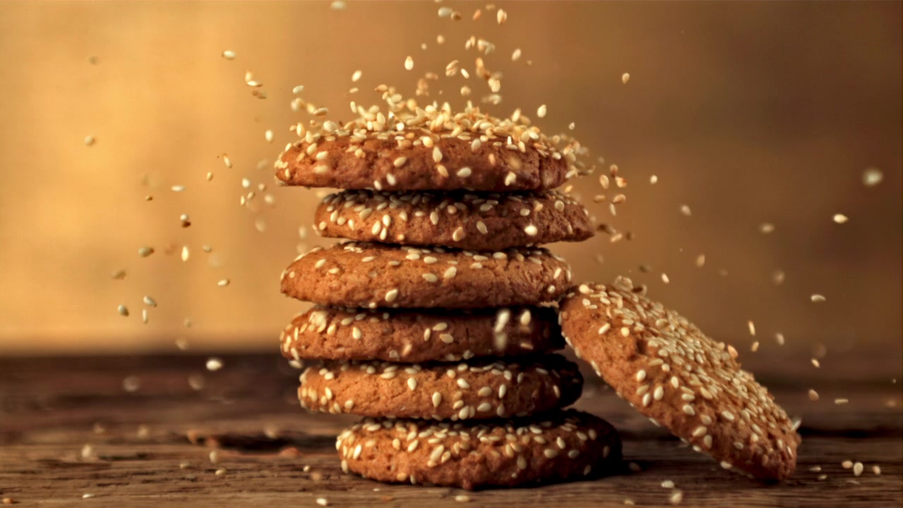 Semi di sesamo che cadono al rallentatore su una pila di biscotti.