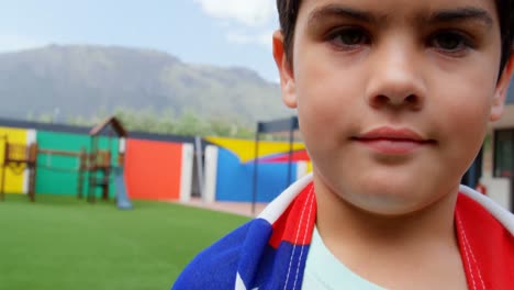 vista frontal de un escolar caucásico envuelto en la bandera estadounidense en el patio de recreo de la escuela 4k