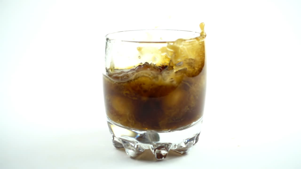 Cubetti di ghiaccio cadono in un bicchiere con una Coca Cola. Rallentatore.