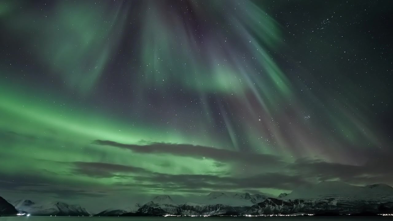 Aurora Boreale Vibrante che Danza su Montagne Innevate e Cittadina Costiera