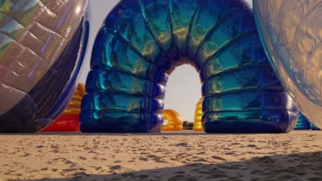 large, colorful inflatable structures create a surreal and playful wonderland on a sandy beach, capturing the essence of summer fun and imagination during the day