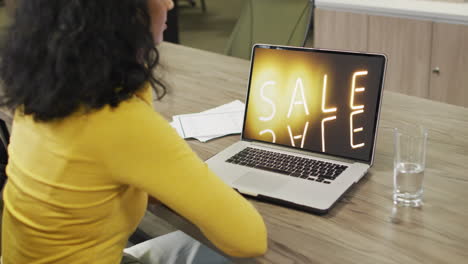 Biracial-woman-at-table-using-laptop,-online-shopping-during-sale,-slow-motion