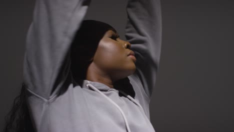 Studio-Portrait-Shot-Of-Young-Woman-Wearing-Hoodie-Dancing-With-Low-Key-Lighting-Against-Black-Background-2