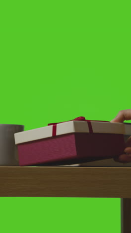 vertical video of man putting present in gift wrapped box onto table shot against green screen