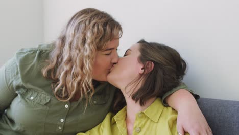 pareja de lesbianas caucásicas besándose y sentadas en el sofá