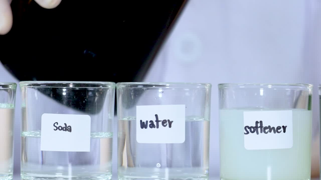 Gros plan d’un liquide bleu versé dans des béchers en verre contenant du soda, de l’eau et de l’adoucissant