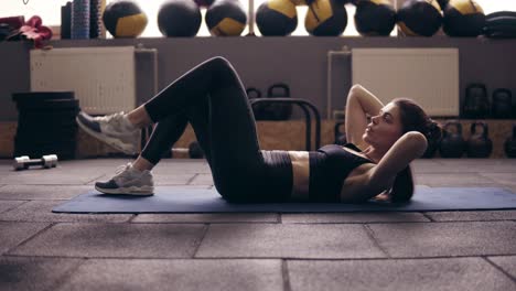 lying abdominal exercises with leg twists performed by sportive brunette girl wearing black sportswear.