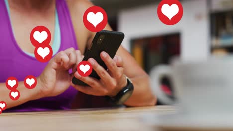 Multiple-heart-icons-floating-against-mid-section-of-caucasian-woman-using-smartphone