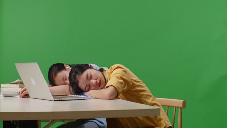 asian woman students sleeping on a table with a laptop while studying in the green screen background classroom