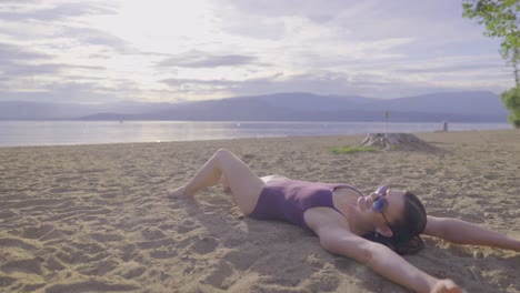 Side-view-of-attractive-girl-doing-sand-angels-on-a-beach