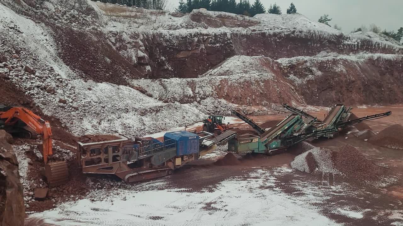 Bulldozer moving around red iron stone inside big quarry during winter