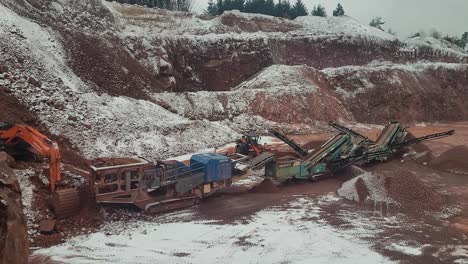 excavadora que se mueve alrededor de piedra de hierro rojo dentro de una cantera grande durante el invierno