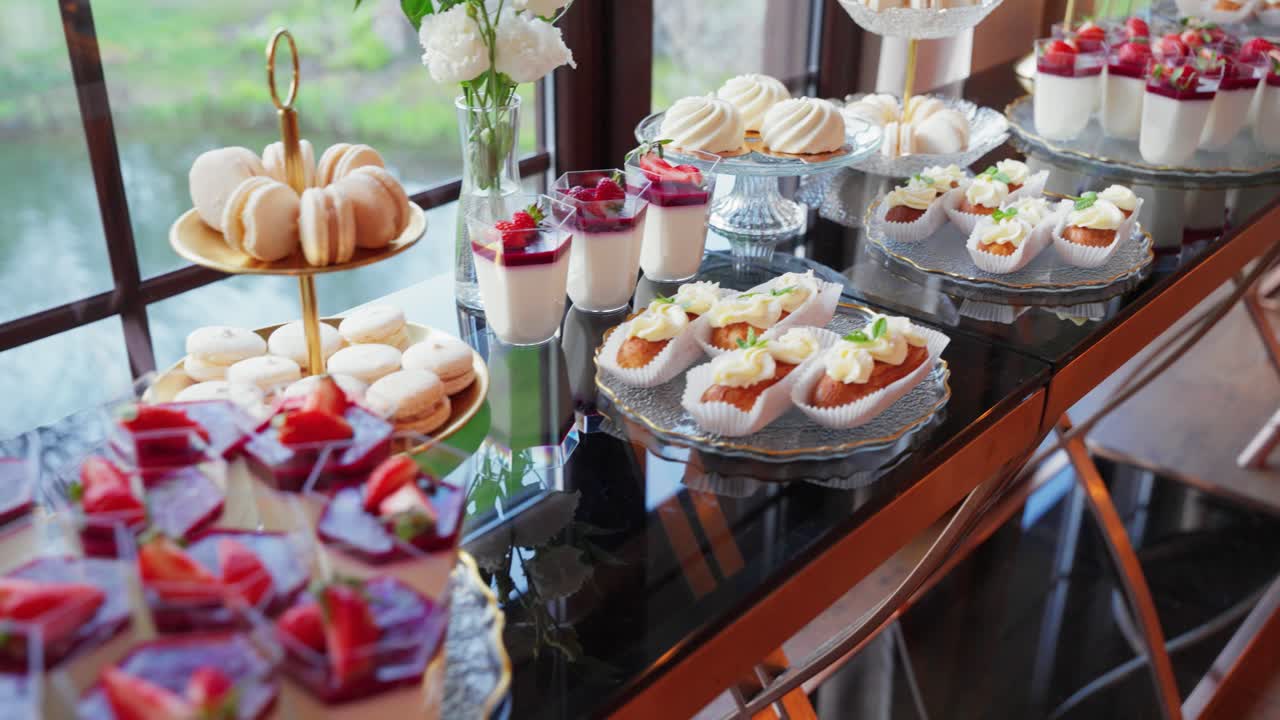 Elegant dessert table with a variety of gourmet sweets including panna cotta, macarons, mini cakes, and fruit desserts beautifully arranged for a wedding or upscale celebration