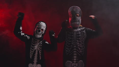 Studio-Shot-Of-Children-Dressed-Up-In-Skeleton-Costumes-Trick-Or-Treating-At-Halloween-Dancing-In-Front-Of-Red-Smoke-Background-Lighting-3