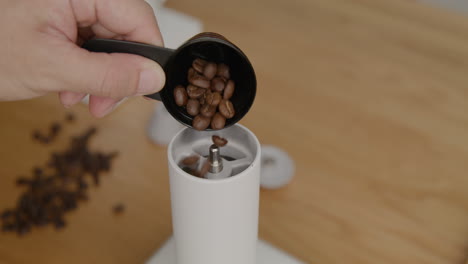 portioning ungrounded coffee beans into the hand grinder with a coffee beans scoop, close up shot on tripod with no movement