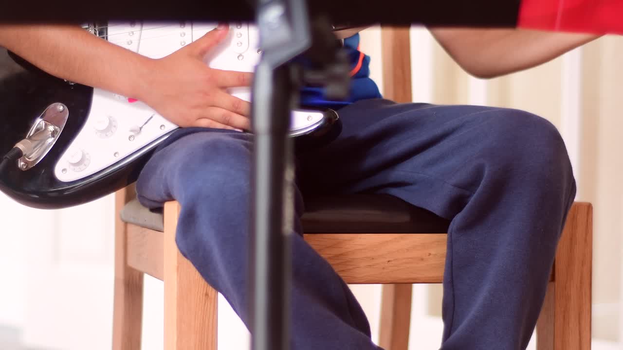 A young boy (school age) practicing on the electric guitar at home with a microphone and music stand in front.