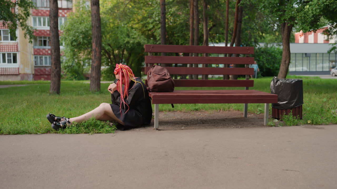 화려한 드레드락을 한 여성이 야외에 조용히 앉아 있어요. 활기찬 머리를 한 외로운 소녀가 근처에서 편안하게 쉬고 있는 도시 풍경이고요. 밝은 드레드락을 한 십 대 소녀가 벤치 옆 공원 가장자리에 혼자 앉아 쉬고 있어요.