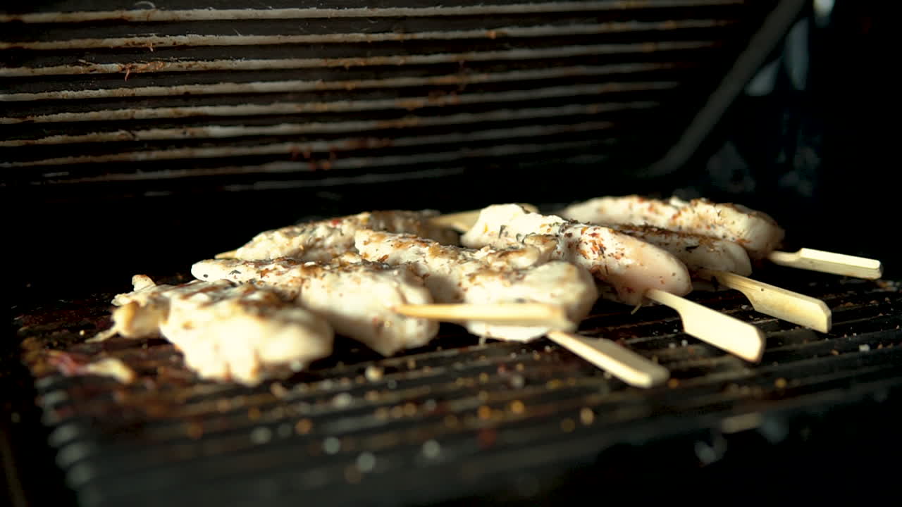 close-up Closing the lid of the grill, chicken pieces stuffed on a wooden stick, slow motion