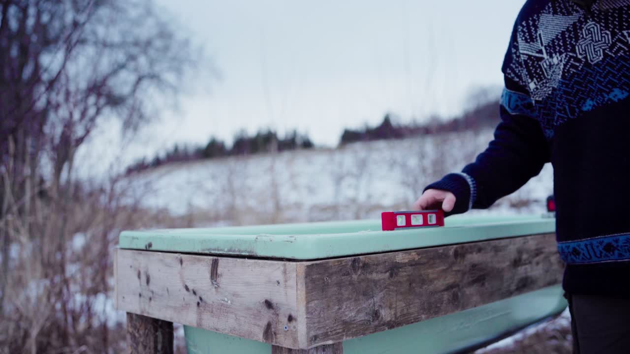 A Man is Using a Level to Ensure the Surface of the DIY Hot Tub is Even - Static Shot