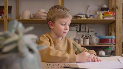 blond kid drawing sitting at a table in a craft workshop 2