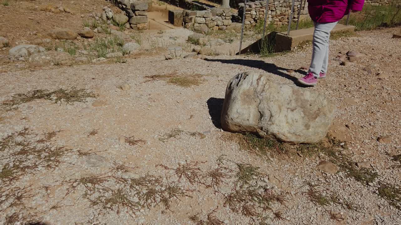 Woman’s legs walking past last rock to give scale in barren landscape