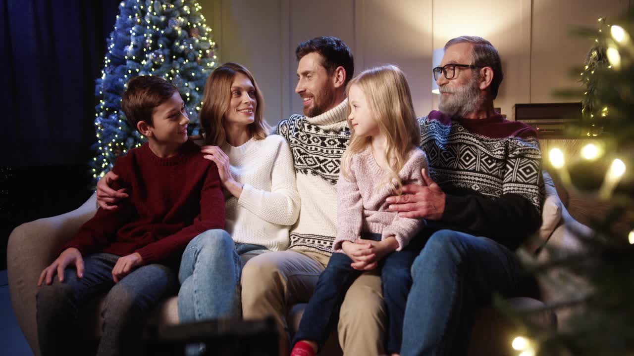 크리스마스 이브에 웃고 장식된 빛나는 크리스마스 트리 근처의 아늑한 집에 함께 앉아 쾌활한 가족을 닫습니다.