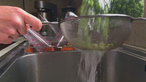 footage of woman washing and rinsing green peas with inox colander in a sink slow motion