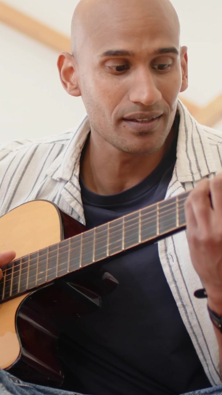 Video verticale: Allontanare la telecamera mostrando un uomo che strimpella la chitarra e canta sul divano per un ascoltatore