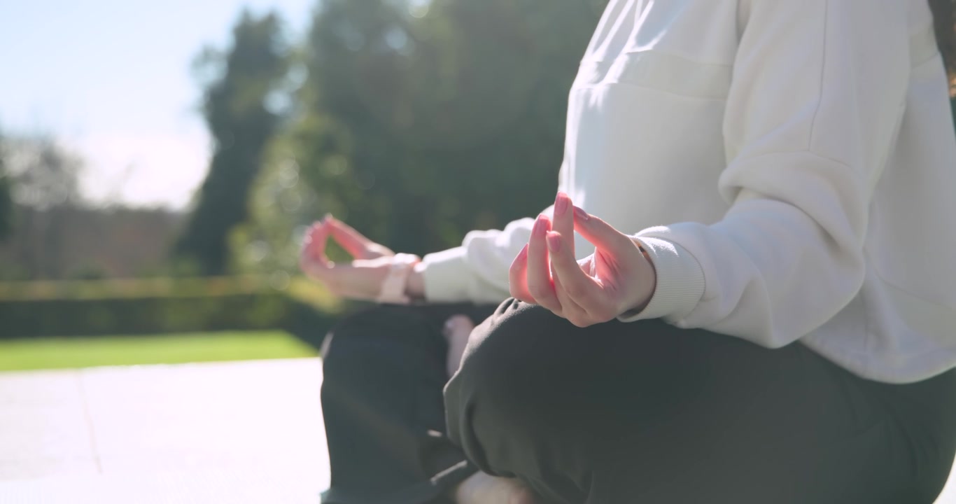Due amiche sedute su un tappetino da patio che tengono un mudra, la luce solare ispira la respirazione, orologio visibile.
