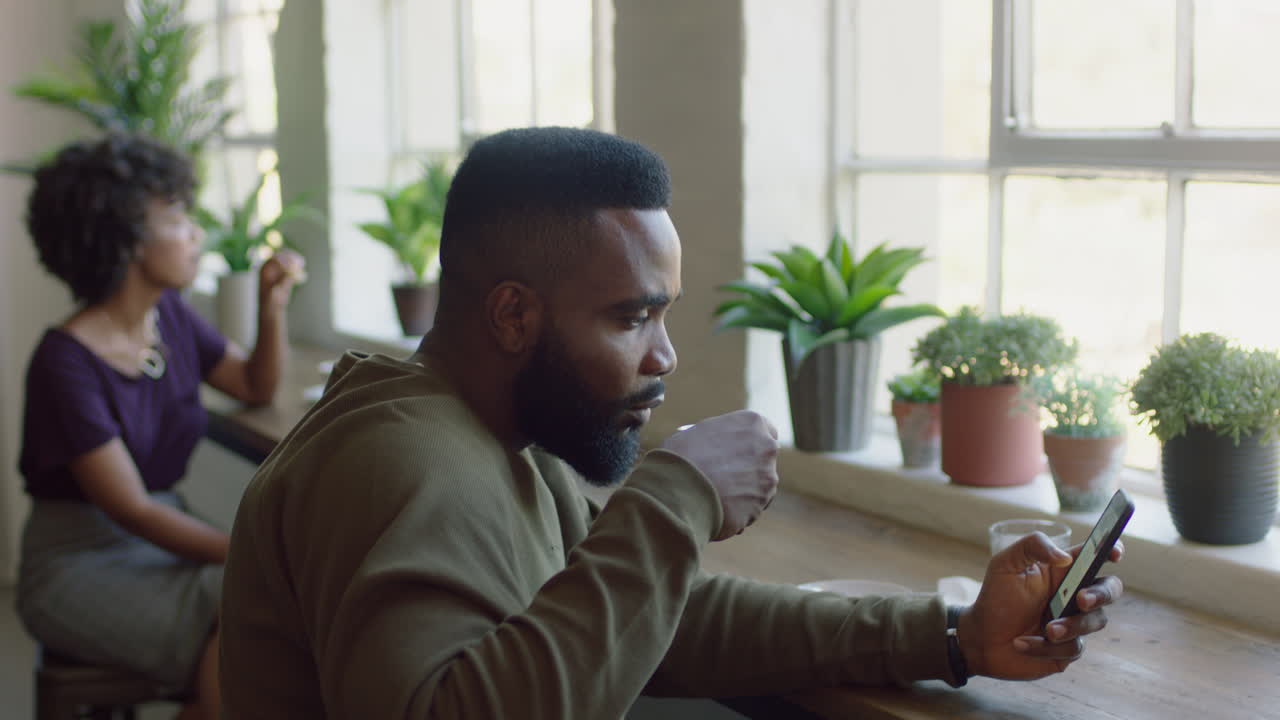 young african american man using smartphone in cafe drinking coffee browsing online messages texting sharing lifestyle on social media enjoying mobile phone