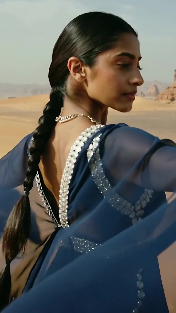 Video verticale: Donna che volteggia in abito blu navy, sventolando le maniche tra le dune, rivelando una catena d'oro e una treccia.