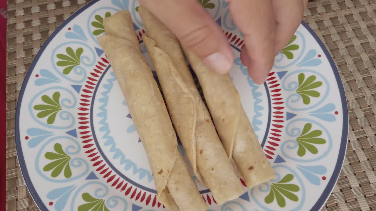 Top down shot hands putting taquitos (taco dorado) on a plate, indoor