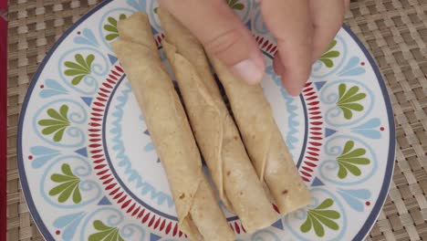 top down shot hands putting taquitos (taco dorado) on a plate, indoor
