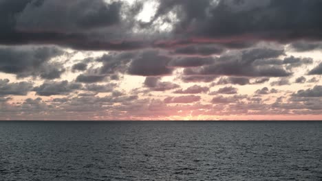 Impresionante-Vista-De-La-Puesta-De-Sol-Detrás-Del-Horizonte-Del-Mar,-Vista-Panorámica-De-Las-Nubes-Y-Las-Olas-Al-Atardecer,-Lapso-De-Tiempo