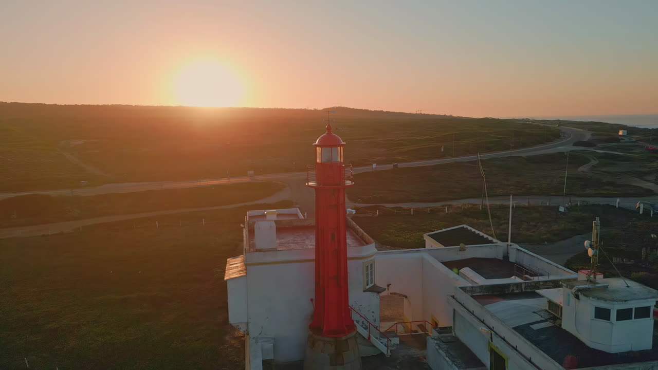 Golden sunset illuminating lighthouse on ocean shore aerial view. Majestic sun