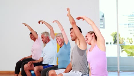 Fitnessgruppe-Sitzt-Auf-Gymnastikbällen-Und-Streckt-Die-Arme-Aus