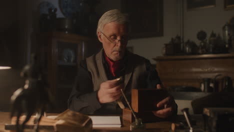 older passionate man evaluates an old watch in his office at night