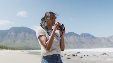 african american woman taking photos with digital camera at the beach