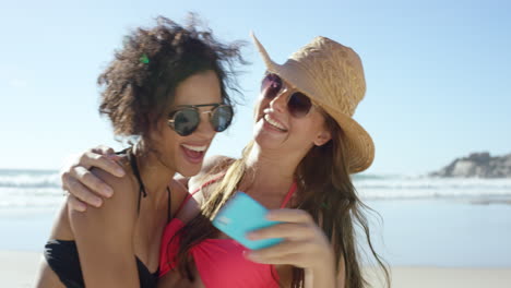 Two-girl-friends-taking-selfies-giving-kiss-on-cheek-on-the-beach