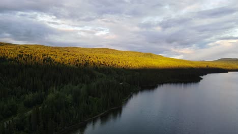 Beautiful,-soft-sunlight-hitting-the-top-of-a-forest-treeline-surrounding-Dease-Lake-in-British-Columbia,-Canada