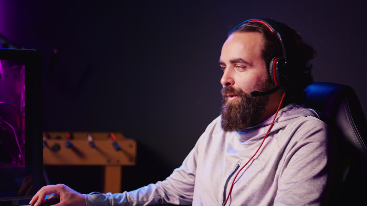 Smiling man plays online multiplayer spaceship videogame with friends, chatting using headphones mic