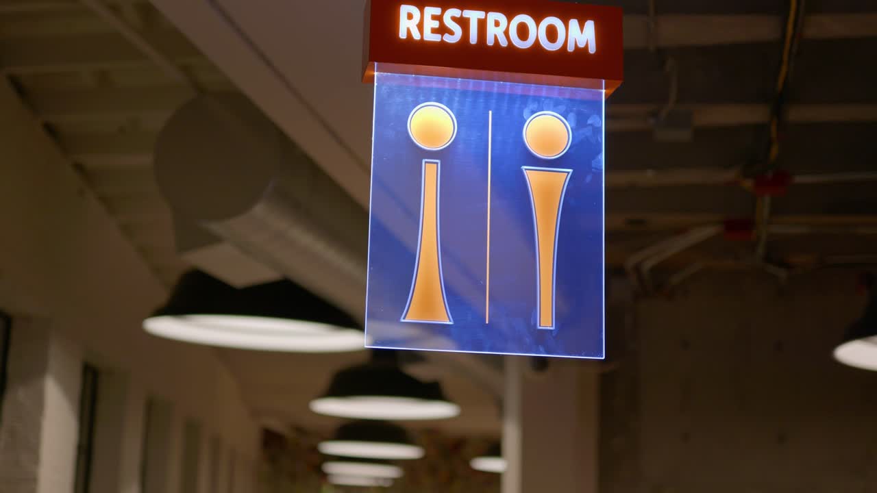 Restroom sign stock clip of a fancy upscale modern design sign that&rsquo;s lit up with led lights up tall on ceiling in industrial venue event studio hall building with huge lamps in background