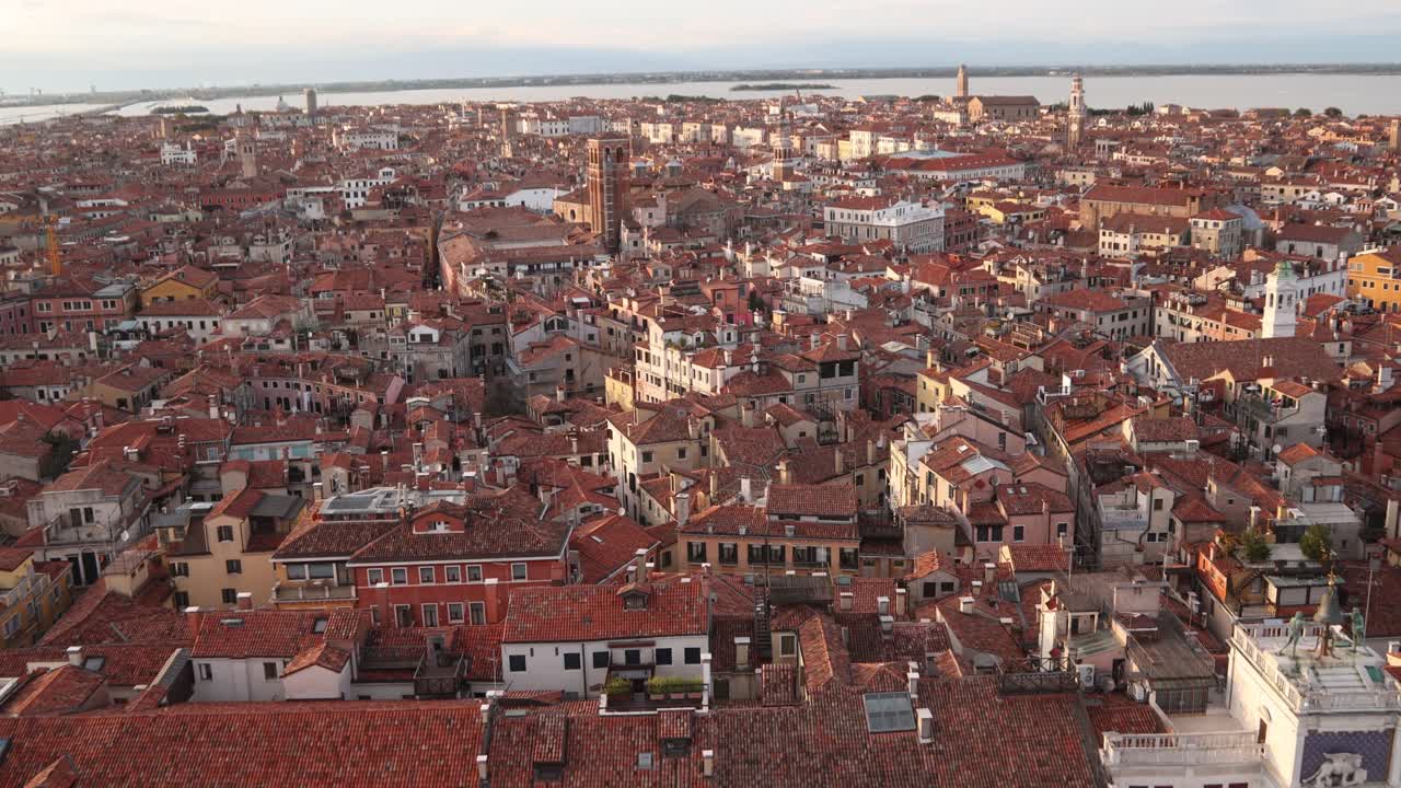 Venice's terracotta rooftops glow in warm sunlight over a sprawling cityscape at sunset