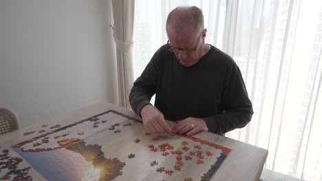 mature man with focused intent to put a large picture puzzle together in his lonely home