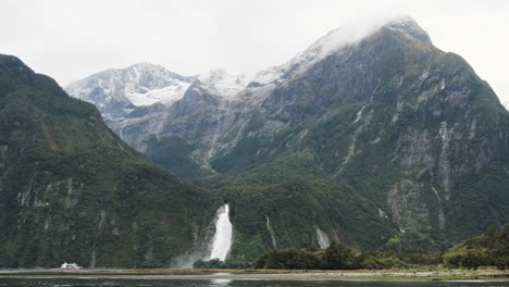 a red ship appears small compared to the majestic beauty of milford sound in new zealand