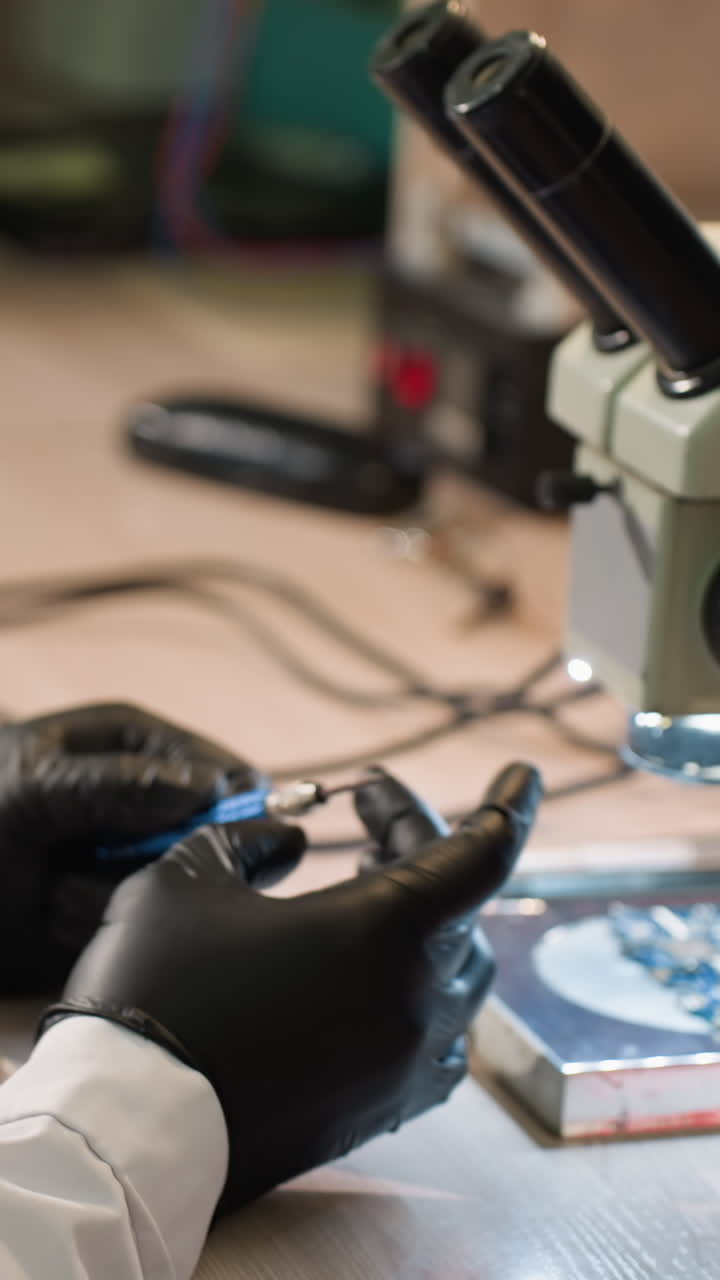 vista de cerca de un técnico en una bata de laboratorio ajustando un tornillo en su mano con un componente electrónico bajo un microscopio y varias herramientas en la mesa y otras cosas en el estante