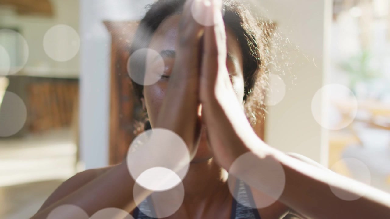 Donna che abbassa i palmi delle mani dall'alto verso il viso in una routine di benessere domestica, luci bokeh sul viso.