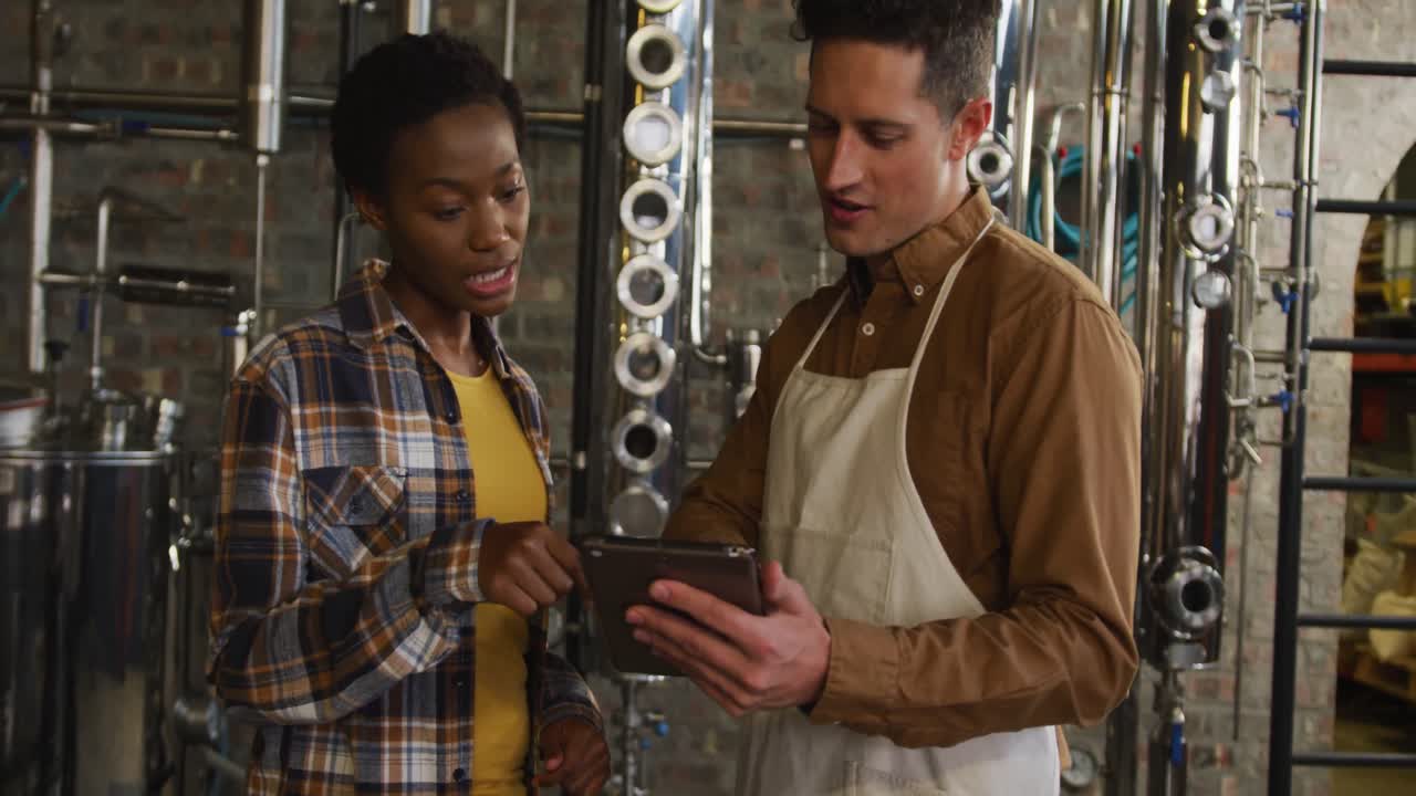 colegas masculinos y femeninos diversos en la destilería de ginebra usando tableta, hablando y sonriendo
